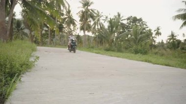 Beyaz gömlekli adam, Scooter 'la Tropikal Ada' daki Boş Beton Yolu 'nda Palm Trees ve Hills' te, geniş açılı manzaralı, Ada Özgürlük Konsepti.