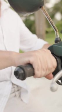 Dikey video. Beyaz Gömlekli Adam, Sunny Yolu 'nda, Arka planda Palmiye Ağaçları, Yan Açı Yakalamada Yolculuk, Özgürlük ve Seyahat Konseptinden Önce Bir Anı Yakalıyor.