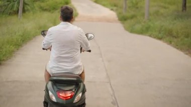 Grass ve Gentle Hills 'in sardığı kırsal bir yolda scooter süren adam, Geri Bakış Yakalayıcı Mesafe ve Basitlik, Kırsal Yolculuk