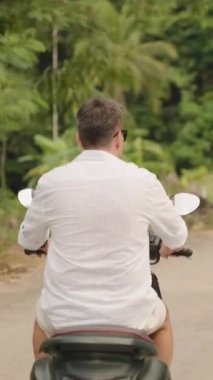 Dikey video. Motosikletli Adam Yoğun Yeşillik, Merkezli Arka Görünüm, Tropikal Keşif Konsepti ve Yoğun Yeşillik Ormanı 'nda Kavisli Yol' a Doğru Sürüyor