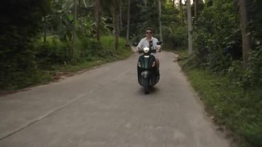 Scooter 'ı Orman Yolu' ndaki kameraya doğru süren adam yemyeşil sebzeli, far açık frontal geniş açılı, Eco Travel Concept