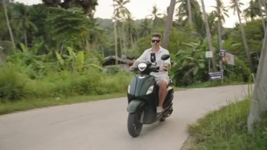 Uzun Palmiye Ağaçları ve Uzak Tepeler, İleri Hareketli Hafif Açı, Tropikal Macera Konsepti ile çevrili Scooter Çevresindeki Adam