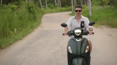 Güneş Gözlüklü Adam Dar Beton Yolu 'nda Skuter sürüyor Palmiye Ağaçları ve Çimenli, Merkezli Düşük Açı Görünümü, Boş Zaman ve Doğa Seyahati Konsepti