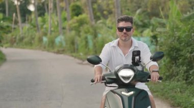 Güneş Gözlüklü Adam 'ın Yakın Çekimi ve Beyaz Gömlekli Scooter Tropikal Yol Boyunca, Orman Arkaplanı, Yavaş Hareketli Ön Çekim, Ada Özgürlüğü Konsepti