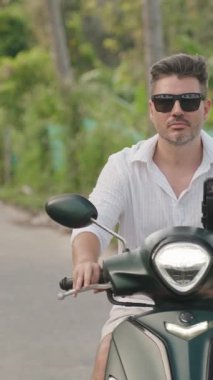 Dikey video. Güneş Gözlüklü Adam 'ın, Tropikal Yeşil Alan' da Scooter sürüşünün, Yavaş Hareket 'te Orman Kuşatılmasının, Huzurlu Seyahat Konseptinin Yakın Çekimi