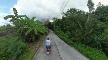 Dar Beton Yolu 'nda Scooter' da Uçan Adam Etrafı Lush Tropikal Ormanı, Yüksek Açı Drone Vuruşu, Orman Arazisinde Seyahat Macerası