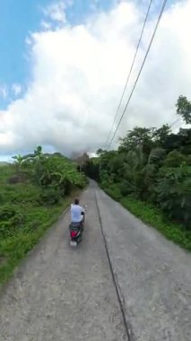 Dikey video. Dar Beton Yolu 'nda Scooter' da Uçan Adam Etrafı Lush Tropikal Ormanı, Yüksek Açı Drone Vuruşu, Orman Arazisinde Seyahat Macerası