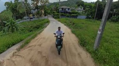 Scooter 'daki adam, Tropikal Orman, Orta Yol, Kırsal Seyahat ve Keşif Aracı ile Hillside Yolu' ndaki Köye doğru gidiyor.