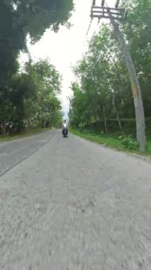 Dikey video. Orman Yolu 'nda Yeşillik ve Dağ Arkaplanında Scooter Binen Adam, Ön, Çevre Seyahati ve Macera Aracından Orta Yol İnsansız Hava Aracı