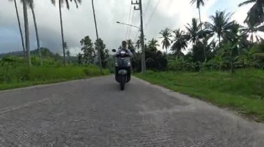 Virajlı yolda Scooter süren adam Tropikal Palmiyeler ve Yoğun Yeşillik ile çevrili, Önden Orta Yol Drone Atışı, Sahne Adası Seyahati