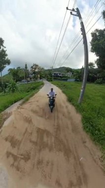 Dikey video. Scooter 'daki adam, Tropikal Orman, Orta Yol, Kırsal Seyahat ve Keşif Aracı ile Hillside Yolu' ndaki Köye doğru gidiyor.