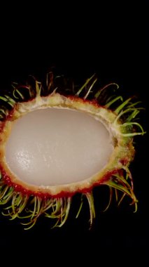Dikey video. Beyaz Etin ve Kırmızı Dikenli Kabuğun Egzotik Taze Meyve Kavramının Yavaş Hareketinde Siyah Arkaplanı Gösteren Makro Görünümünde Rambutan Dönüşünü Aç