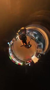 Dikey video. Minik Gezegen Görünümlü Scooter Sürücüsü Gece Şehrinde Sürüş Işık İzleri ve 360 derecelik Gerçeküstü Seyahat Macerası Kamerası Efekti