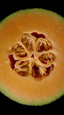 Dikey video. Turuncu Et ve Kümelenmiş Tohumlar ile Kavun Çapraz Bölüm Üst Görünümü Kusursuz Dönüşümlü Siyah Arkaplanda İzole