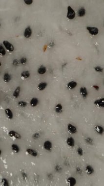 Dikey video. Dönen ve Düşen Ejder Meyvesinin Dolly Kaydırıcısının Yakın Çekimi Siyah Arkaplana Karşı Havada Siyah Tohumlar ve Parlak Pembe Deriyle Beyaz Etleri Gösteriyor