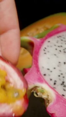 Dikey video. El Tutuşunun Dolly Kaydırıcısı Yarı Tutku Meyvesi Sulu Sarı Pulp ve Siyah Yüzeyde Ejderha Meyvesi Tohumlarını Gösteriyor