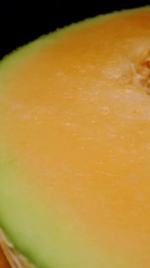 Dikey video. İki Kavunlu Kavun 'un Dolly Kaydırma Çekirdeği Siyah Arkaplana Karşı Dokulu Kabuk ve Temiz Kesikli Sulu Portakal ve Tohum Çekirdeğini Gösteriyor