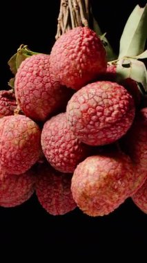 Dikey video. Terkedilmiş Kara Arkaplan 'a Karşı Kusursuz Döngüde Dönen Yapraklarla Olgun Meyveler Kümesi, dramatik ışıklandırma, Tropikal Hasat ve Egzotik Meyve Konsepti ile yakın plan çekimleri