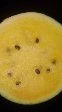 Dikey video. Görünür Tohumlar ve Sulu Et ile Siyah Bir Arkaplan Karşısında Kusursuz Dönen Sarı Karpuz Çekimi