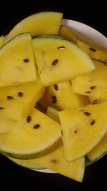 Dikey video. Siyah arka planda dönen yeşil karpuz dilimli tabaklar tatlı atıştırmalıklar ve sağlıklı yiyecek konsepti