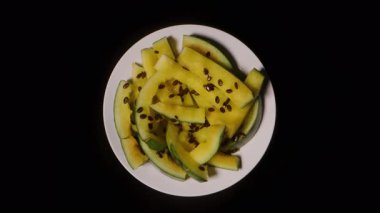 Yediğimiz Sarı Karpuz Kabuklarıyla Dönen Beyaz Tabak Görünümü ve Siyah Arkaplanda Dağılmış Tohumlar Kalan Meyve Kalıntılarını Vurguluyor