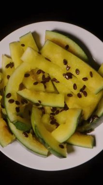 Dikey video. Yediğimiz Sarı Karpuz Kabuklarıyla Dönen Beyaz Tabak Görünümü ve Siyah Arkaplanda Dağılmış Tohumlar Kalan Meyve Kalıntılarını Vurguluyor