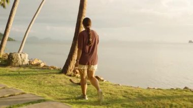 Palm-Lined Shore 'da Durgun Okyanusa Bakan Kadın Gün batımında Uzaktaki Dağlarla, Manzaralı Yansıma Konsepti