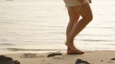 Sahil şeridi boyunca yavaşça yürüyen çıplak ayaklı kadın. Gün batımında yanında dalgalar sürükleniyor. Yan Angle 'dan, Huzur Sahil Anı kavramından.
