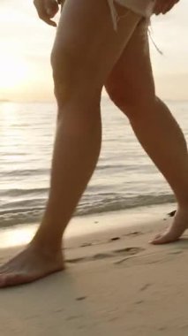 Dikey video. Gün batımı arkasında parıldarken Küçük Kayalıklarla Kumsalda Yürüyen Kadın Rahatlamış Ada Akşam Konsepti