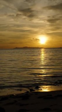 Dikey video. Yumuşak Altın Işık, Sakin Dalgalara Yansıyan Kişi Sahilde Sunset ve Uzak Adalar Arkaplanında, Huzurlu Gece Yürüyüşü Konsepti ile Gezinirken