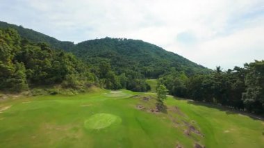 FPV İHA, Parlak Gök Altında Yoğun Tropikal Orman ve Tepeler Arasında Lush Golf Sahasında Uçuyor