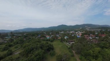 Yoğun Tropikal Ağaçlar ve Mavi Gök Altında Yuvarlanan Dağılmış Bulutlar ve Kırsal Yerleşim Konseptiyle çevrili Küçük Şehir Hava Manzarası