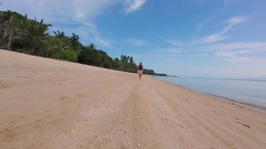 Drone, Parlak Mavi Gökyüzü, Özgürlük ve Keşif Altındaki Sakin Denizi ve Palmiye Ağaçlarını Gösterirken Kumsalda Dolaşan Kadın 'ın Hava Çekimi