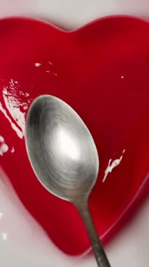 Dikey video. Kırmızı Kalbe Dokunan Kaşık Tabakta Hafifçe Sallanırken, Yavaş Hareket Etkisi, Oyuncu Tatlı Konsepti ile Kapanırken