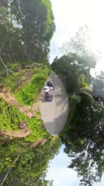 Dikey video. Dar Yoldaki Yoğun Tropikal Ormanda Scooter süren çift Küçük Gezegen Efektiyle Yakalandı