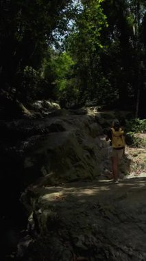 Dikey video. Kadın Gezgin 'in Gün Işığı Altında Rocky Şelalesi Yolu' na Tırmanması, Arka Görüş, Macera Yürüyüşü Konsepti