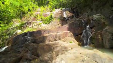 Uçan İnsansız Hava Aracı Orman Şelalesi 'ne doğru ilerliyor. Çevresinde yoğun yeşillik, düşük açılı izleme çekimi, Tayland Doğa Konsepti var.