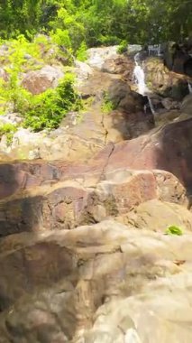 Dikey video. Uçan İnsansız Hava Aracı Orman Şelalesi 'ne doğru ilerliyor. Çevresinde yoğun yeşillik, düşük açılı izleme çekimi, Tayland Doğa Konsepti var.