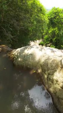 Dikey video. İnsansız Hava Aracı Orman Şelalesi 'ne doğru hızla iniyor Aşağıdaki Rocky Nehir yatağı, Yukarıdaki Dik Açı, Tropikal Tayland Konsepti