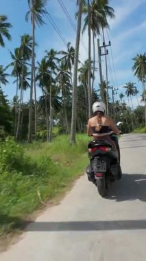 Dikey video. Palmiye Ağaçları, İzleme Çekimi, Tayland Samui Adası Seyahat Konsepti ile çevrili Orman Yolu 'nda Scooter süren Kadın Arka Görünümü