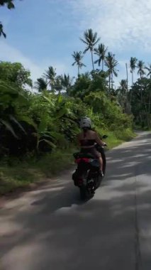 Dikey video. Scooter 'da Kadın Kovalamak Yoğun Tropikal Ormanda Arka planda Dağlar, Düşük Takip Açısı, Tayland Samui Adası Seyahat Konsepti