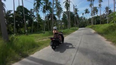 Scooter 'daki kadın, Palmiye ağaçlarının arasından geçerek uzak tepelere doğru gidiyor. Arka alçak açı, Tayland Samui Adası Seyahat Konsepti.