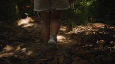 Orman Yolu 'nda Yavaşça Yürüyen Bir Kadın' ın Yakın Çekimi Sıcak Işık Altında Sırt Çantası, Düşük Açı, Yavaş Hareket, Tropikal Ada Keşfi Üzerinde Sneakers ve Shorts Giyiyor