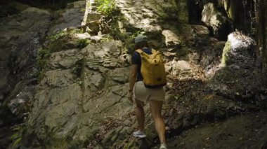 Cap ve Sarı Sırt Çantalı Kadın, Doğal Işık ve Doku, Açık Hava Keşfi Konseptine Odaklanarak Yavaş Çekimde Rocky Ormanı Yolu 'na Tırmanıyor
