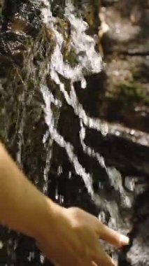 Dikey video. Kadın Elini Küçük Şelaleye Akıyor Yavaş Çekimde Karanlık Orman Kayası, Yan Açı Çekimi, Tazeleme ve Doğa Bağlantısı Konseptinde