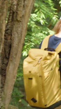 Dikey video. Sarı Sırt Sırtlı Kadın Tayland 'da Yoğun Tropikal Ormanda Yürüyor Destek İçin Asılı Sarmaşığa Tutunuyor Ağaçların Arkasından Vuruldu, Doğal Keşif Konsepti