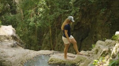 Cap ve Shorts 'lu Kadın Yoğun Orman' da Rocky yamacında Yalınayak Tırmanıyor Ağaçların Arasında Güneş Işığı Süzüyor, Yan Görünüm, Macera Konsepti