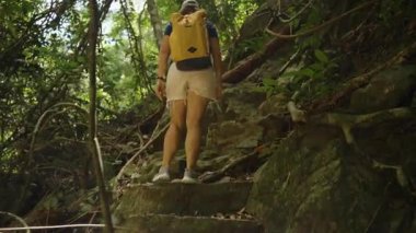 Orman sarmaşıkları ve ağaçlarla çevrili Tırmanan Kadın Sırt çantası ve Spor Ayakkabıları, Düşük Açı, Macera ve Çaba Konsepti