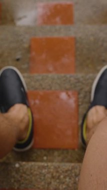 Dikey video. Islak Adam Tropikal Yağmurda Tuğla Basamaklarda Otururken İlk Kişi Açısı 'ndan görülebilen Bacakları, Kırmızı Kiremitlere Düşen Yağmur Damlaları, İlk Kişi Görünümü, Yağmur ve Bekleme Konsepti