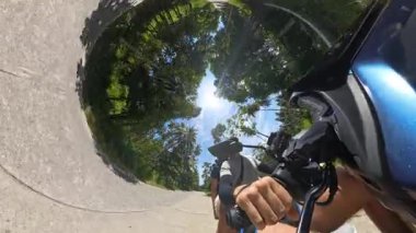 Erkek ve kadın palmiye ağaçlarının altında parlak güneşe doğru scooter sürüyor. Dairesel gökyüzü etkisi, 360 derecelik kamera, tropikal çevre, Ada Yolculuğu Konsepti